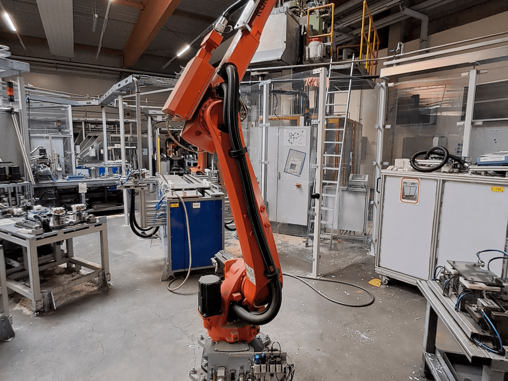 Braccio robotico KUKA KR 26 R3100/SEL in un ambiente industriale, ripreso di profilo con attrezzature operative sullo sfondo.