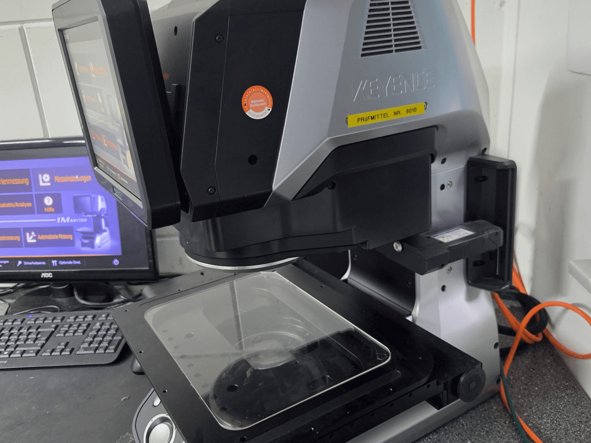 Macchina di misura ottica KEYENCE IM 7030, vista frontale con display touchscreen e piastra di misura in vetro.