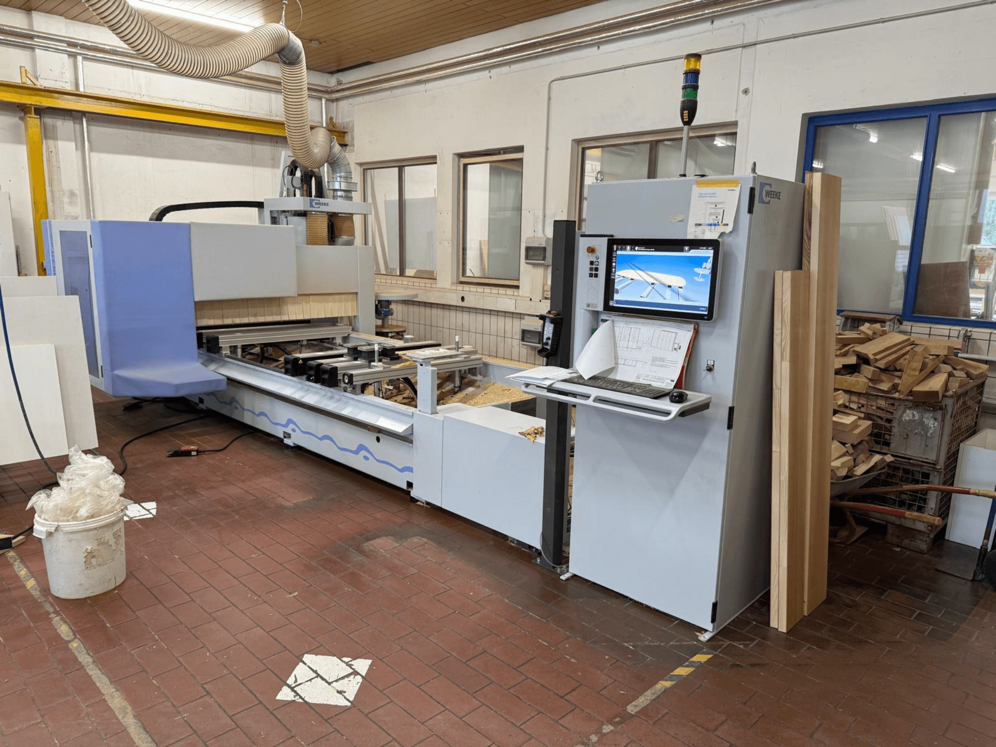 Centro di lavorazione del legno CNC Weeke PROFI BMG211/32/12/K, vista frontale, con pannello di controllo e pezzi di legno, dotato di sistema di aspirazione delle polveri.