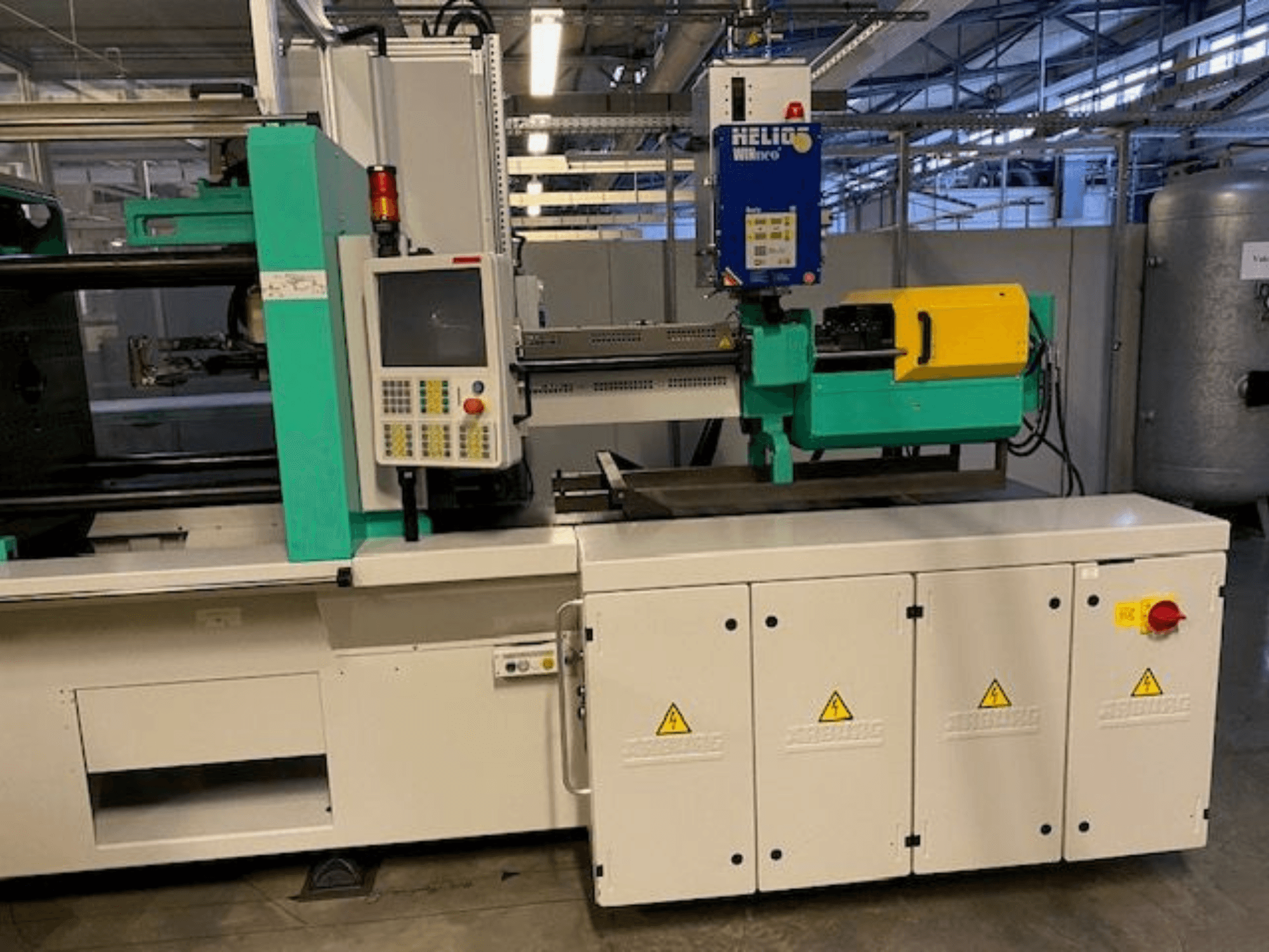 Macchina industriale per lo stampaggio a iniezione, modello HELIO, vista frontale, con pannello di controllo, protezioni di sicurezza e pulsante di arresto di emergenza.