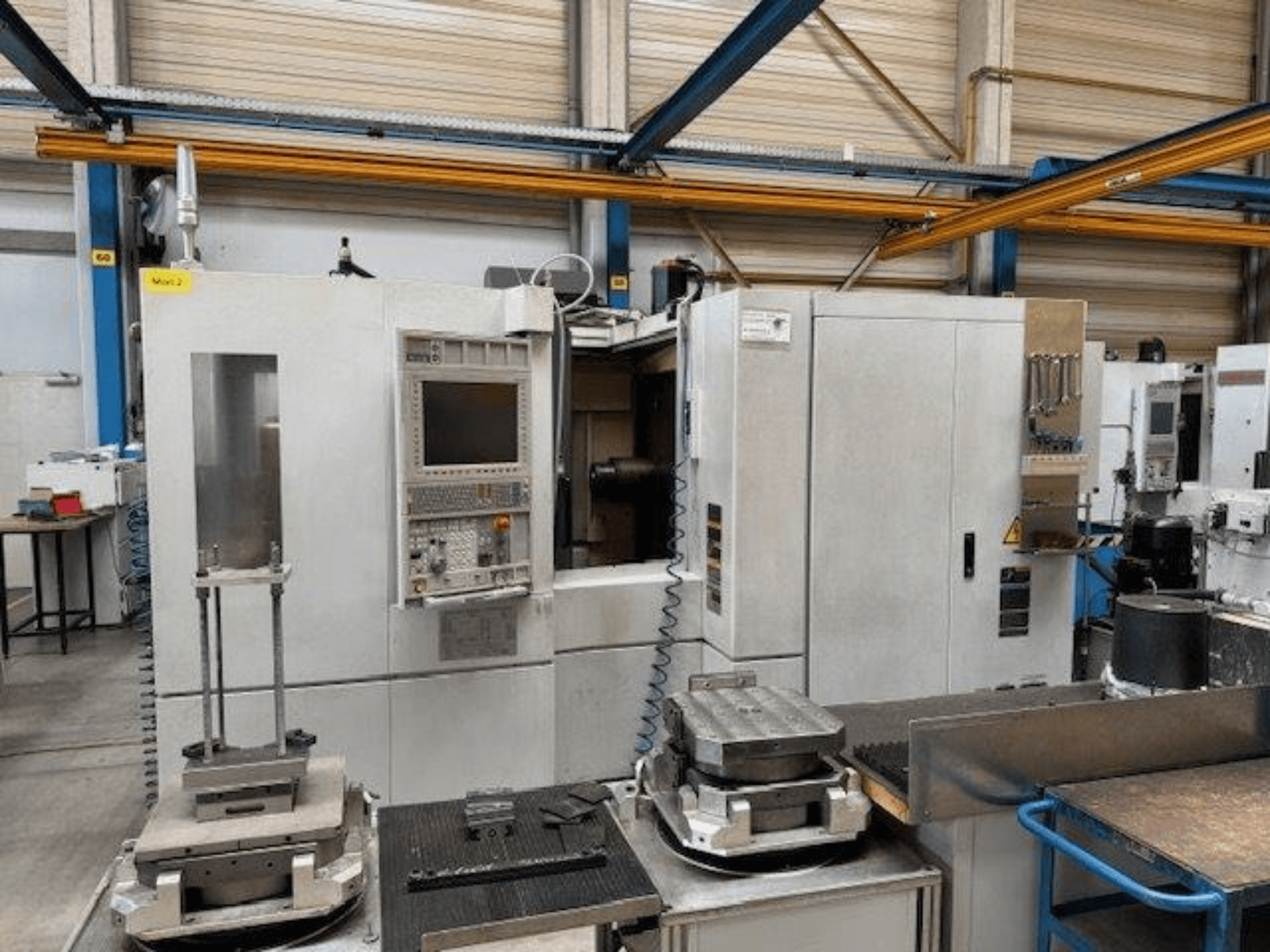 MORI SEIKI NH4000 DCG vista frontale di un centro di lavoro orizzontale con pannello di controllo e pezzi sul tavolo.