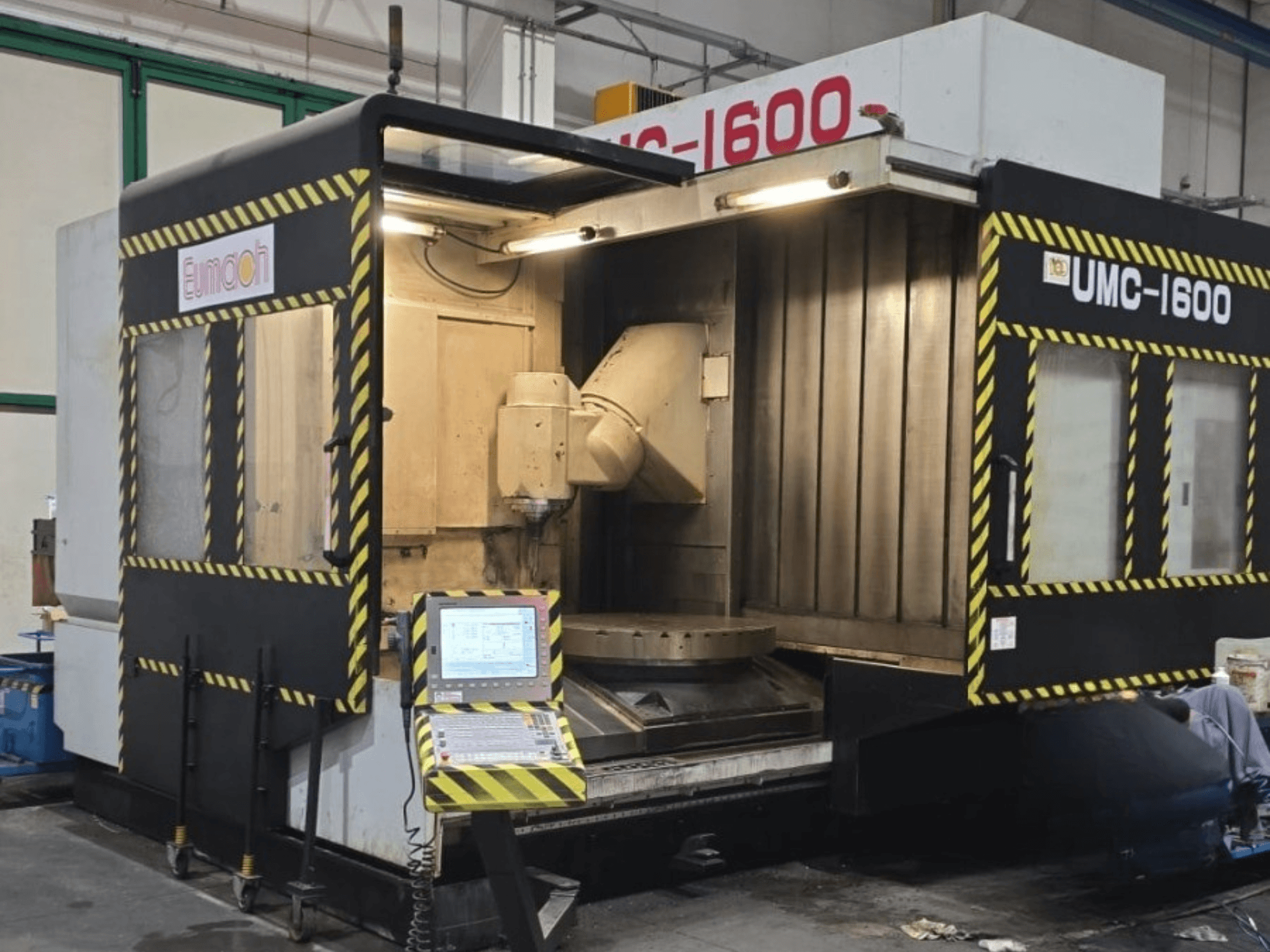 Centro di lavorazione verticale Eumach UMC-1600, vista frontale che mostra i comandi e l'area di lavorazione con le strisce di sicurezza.