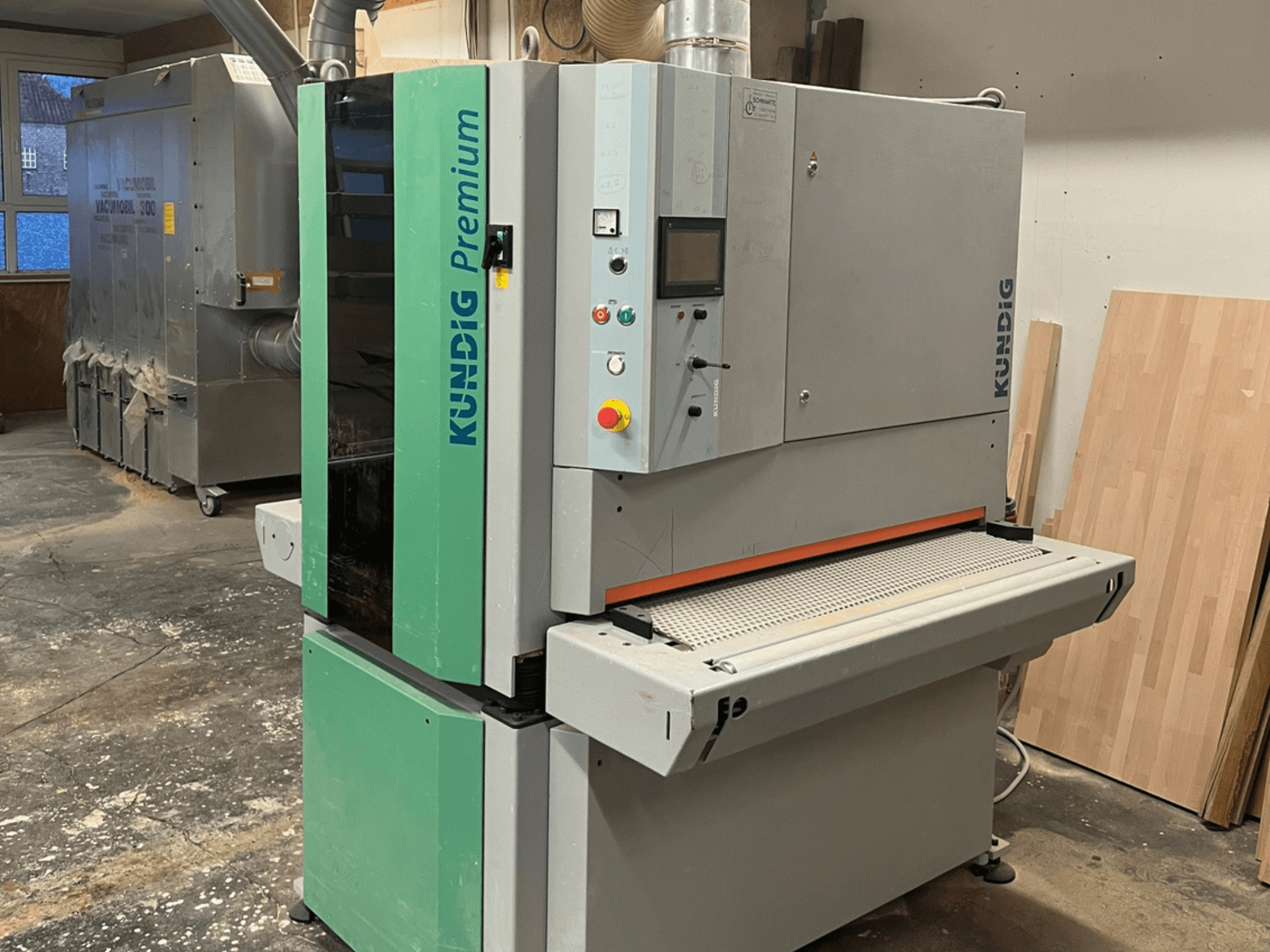 Levigatrice a nastro Kundig Premium-1 1100K in grigio e verde, vista laterale con pannello di controllo e nastro abrasivo visibili.