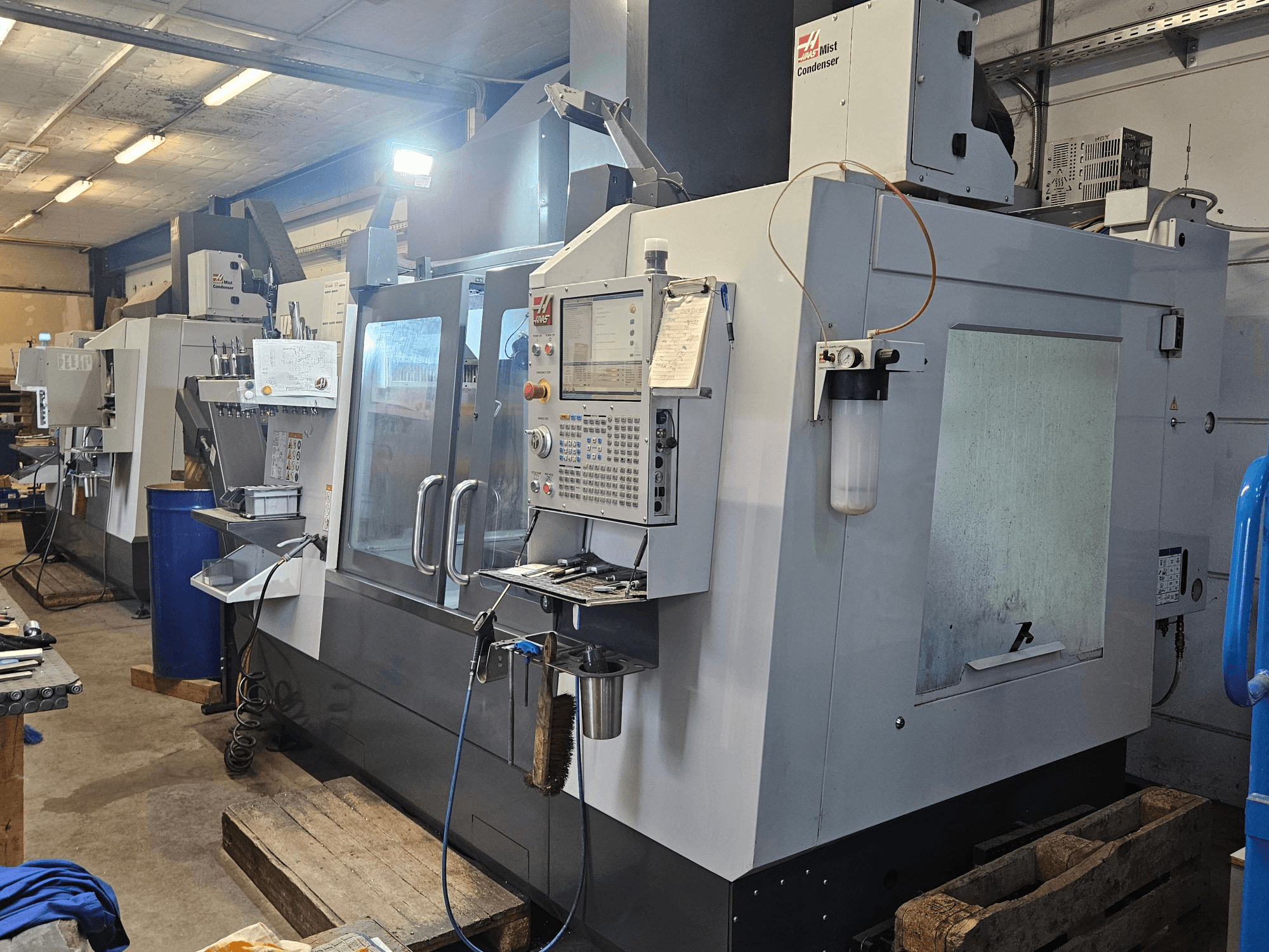 Centro di lavorazione verticale Haas VF-3YT/50 in un'officina, vista frontale che mostra il pannello di controllo, i portautensili e il condensatore di nebbia.