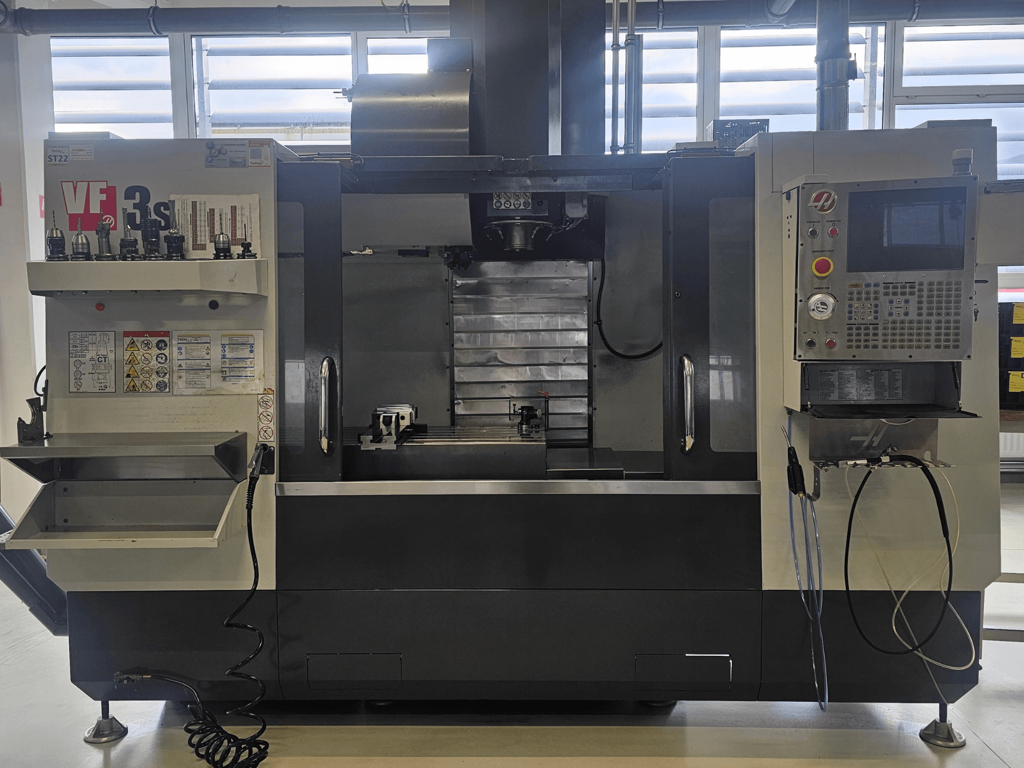 Fresatrice CNC Haas VF3SS, vista frontale, con portautensili, pannello di controllo e vaschetta del refrigerante vuota, con etichette di sicurezza visibili.