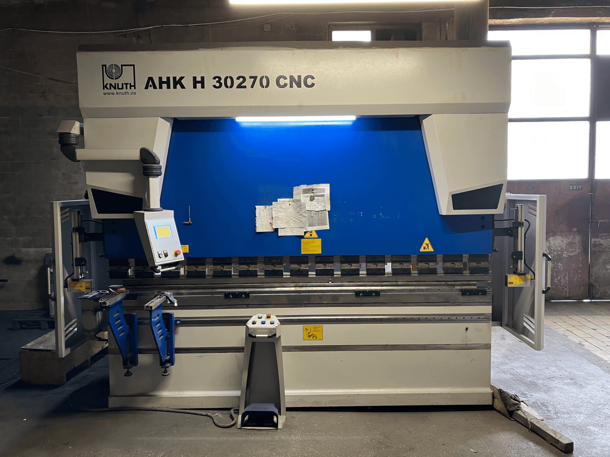 Piegatrice CNC KNUTH AHK H 30270 in un'officina, vista frontale, con pannello di controllo e design blu/bianco, con sportello laterale aperto.