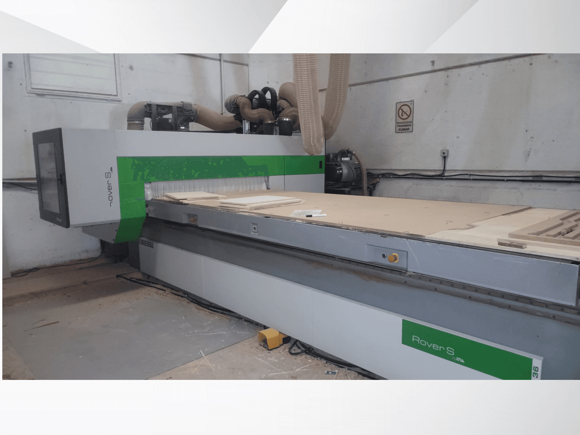Vista frontale della macchina CNC Biesse Rover S, caratterizzata da un ampio piano di lavoro con pannelli in legno e tubi di aspirazione della polvere.