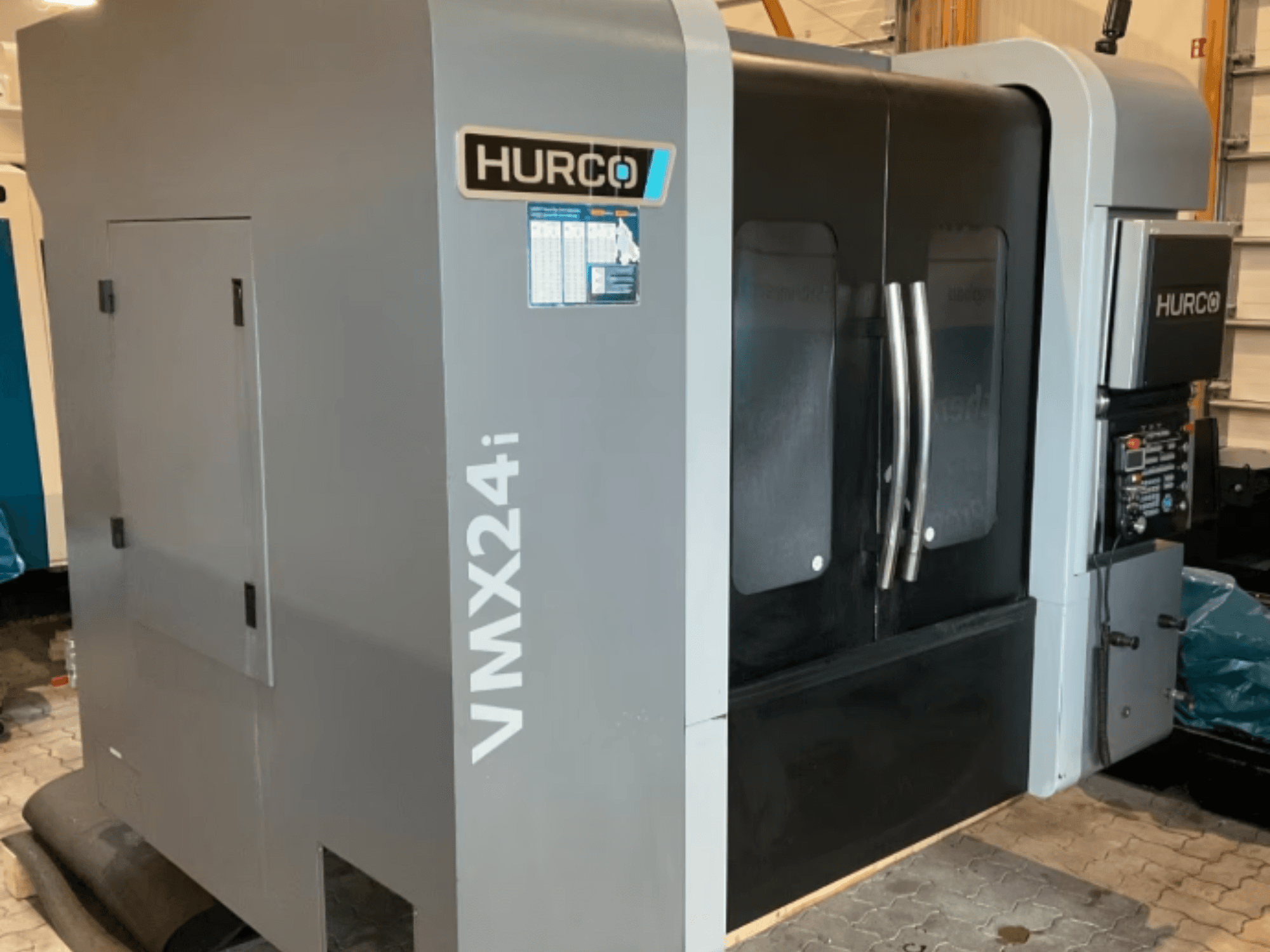Centro di lavoro verticale Hurco VMX 24i, vista frontale con struttura grigio metallizzato, ante dei pannelli nere e interfaccia di comando.