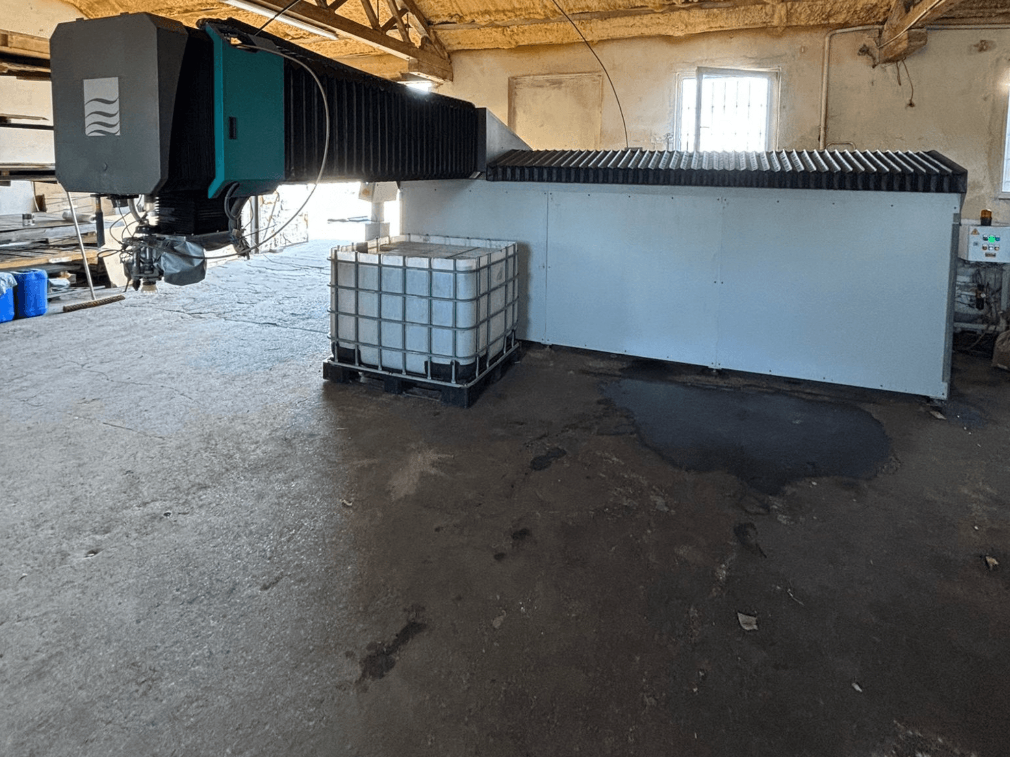 Macchina industriale a getto d'acqua in un'officina, vista laterale, con un grande serbatoio d'acqua e un pannello di controllo visibile accanto.