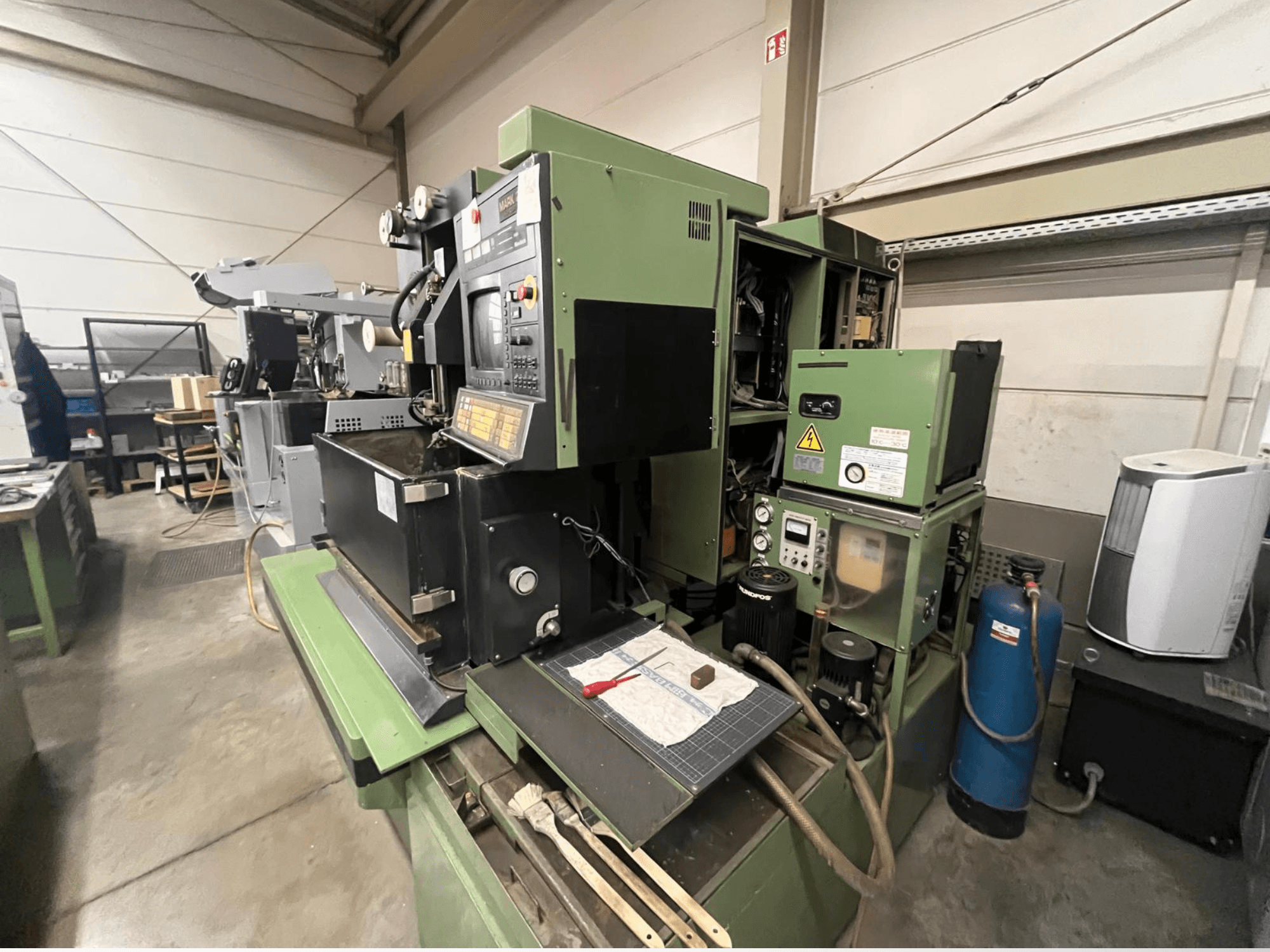 Macchina industriale verde con pannello di controllo, vista laterale; comprende componenti idraulici e superficie di lavoro con utensili.