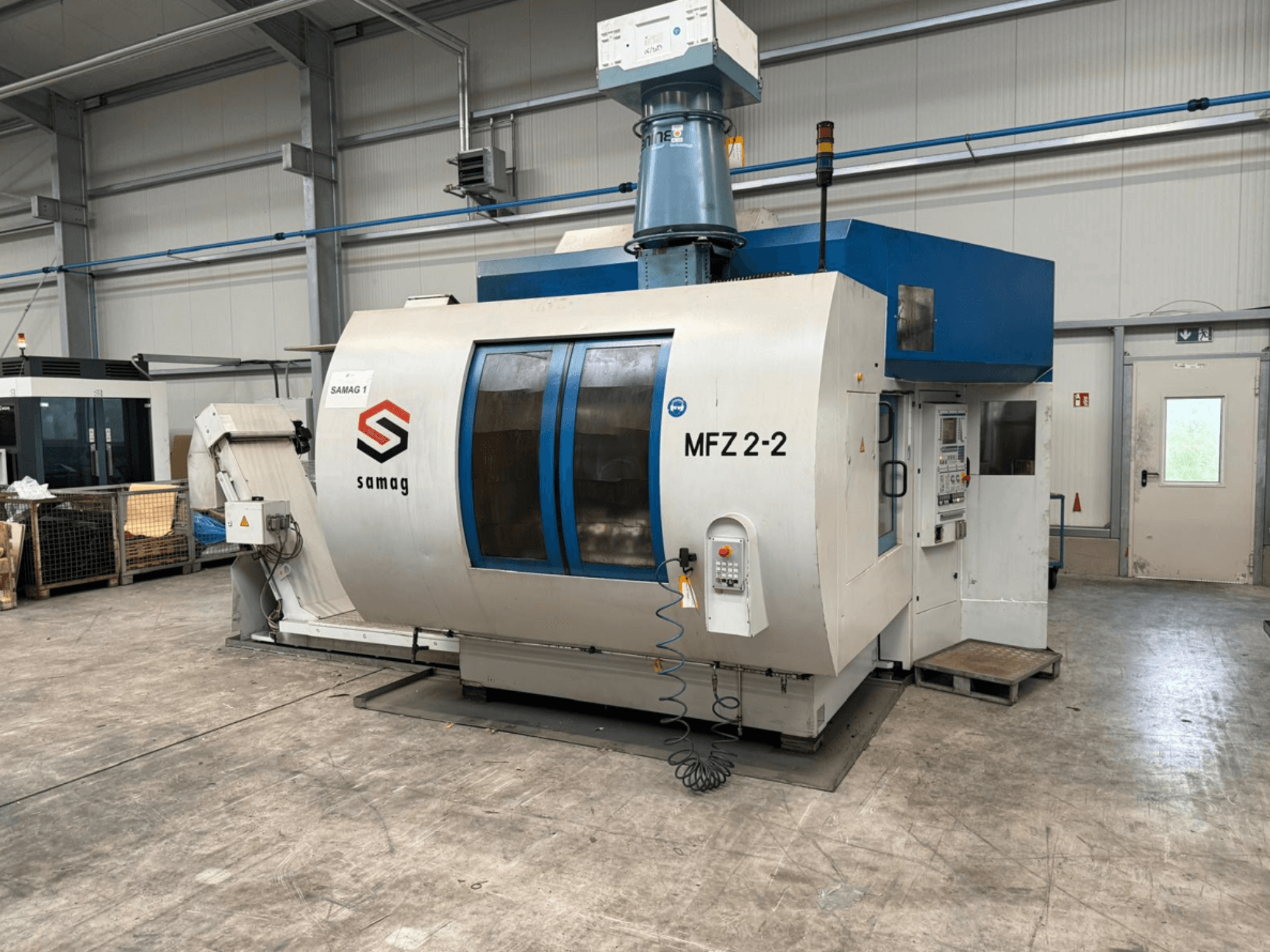 Macchina utensile Samag MFZ 2-2, vista frontale, con pannello di controllo e piano blu, con caratteristiche di sicurezza in un ambiente industriale.