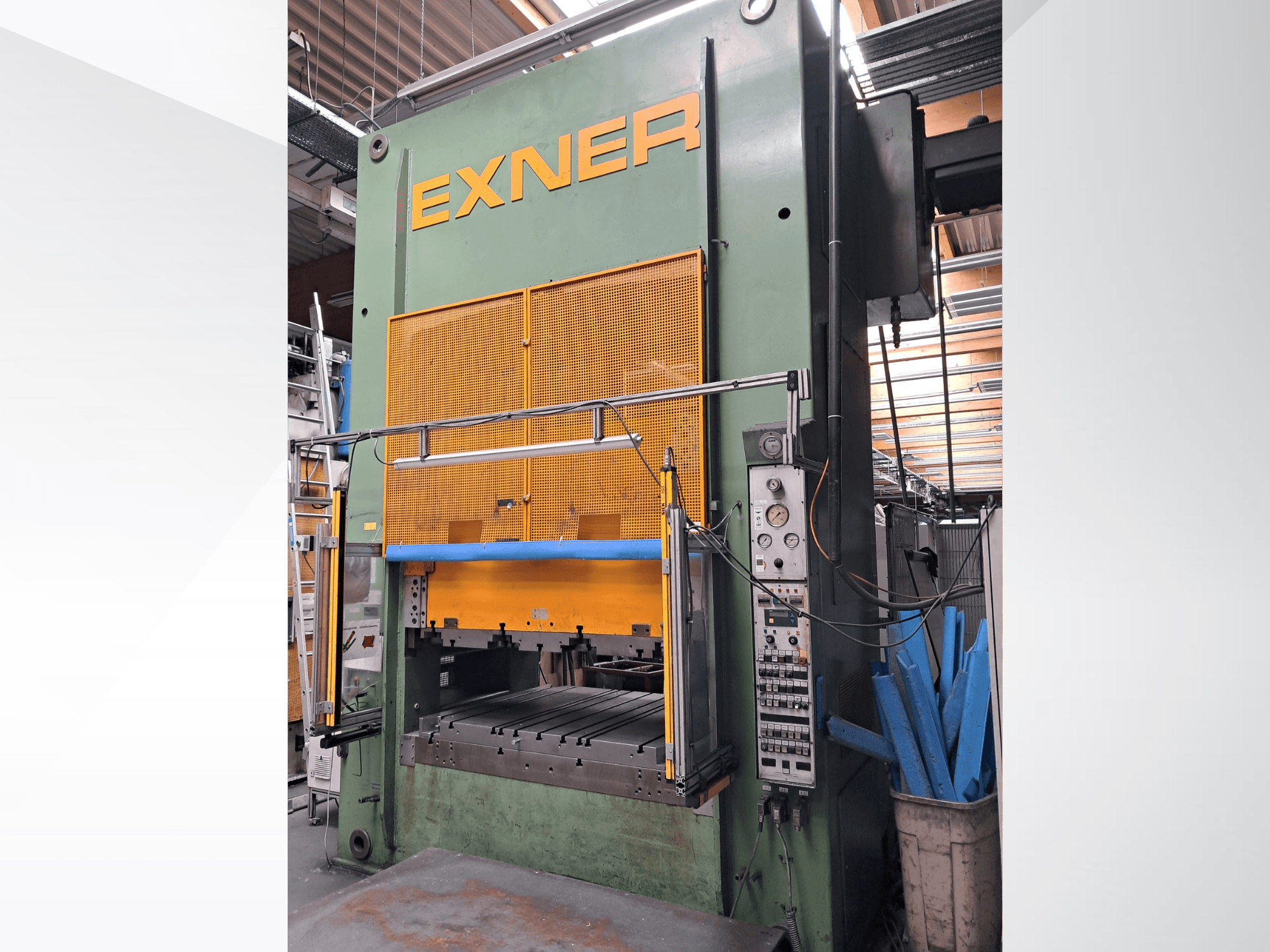 Pressa idraulica EXNER EX SBR 150, vista frontale; dotata di comandi, barra di sicurezza blu e protezione in rete metallica, collocata in un ambiente di officina.