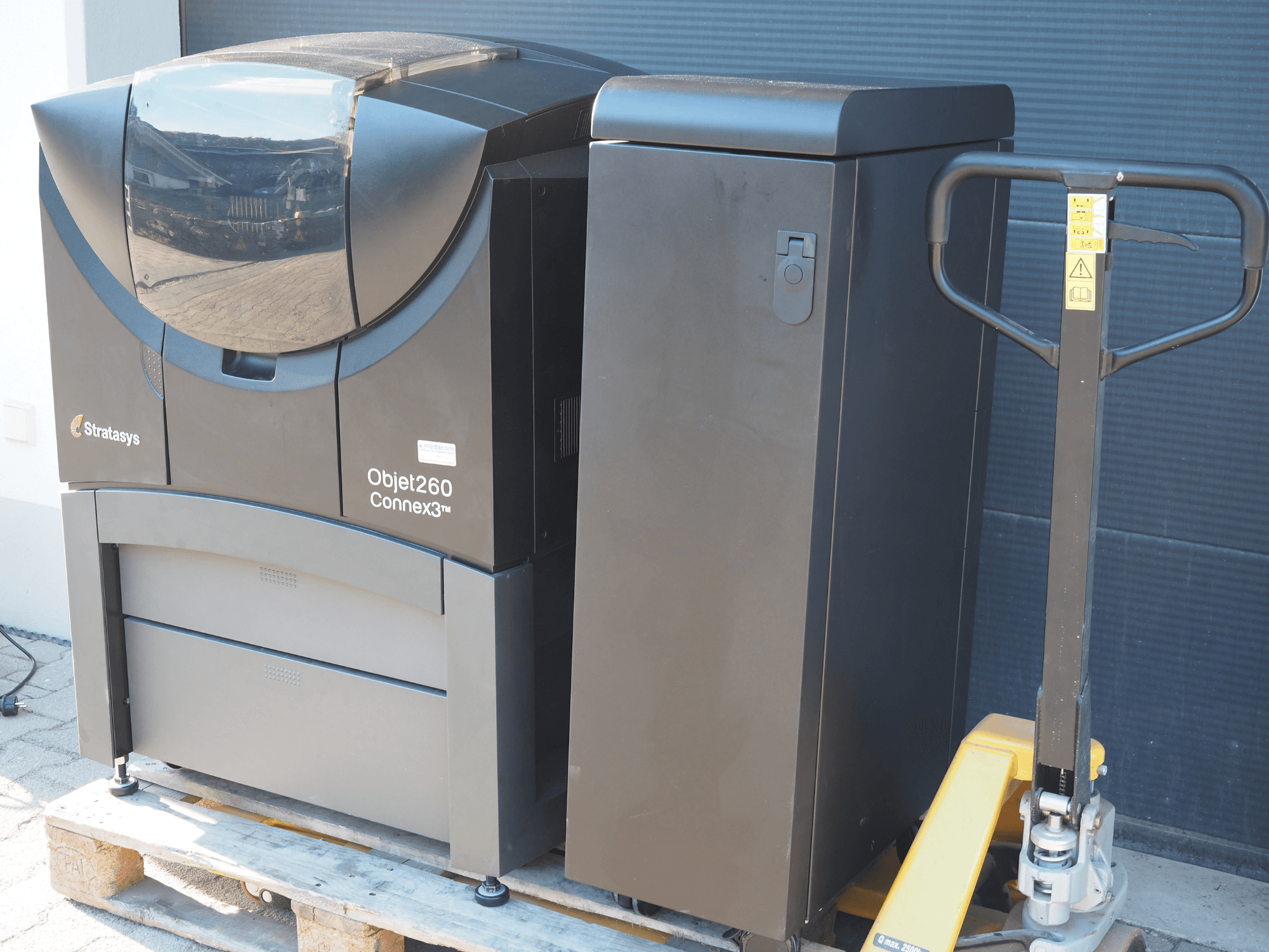 La stampante 3D in plastica Stratasys Objet260 Connex3, vista laterale, presenta un design compatto con pannello di controllo e contenitore di materiale collegato.