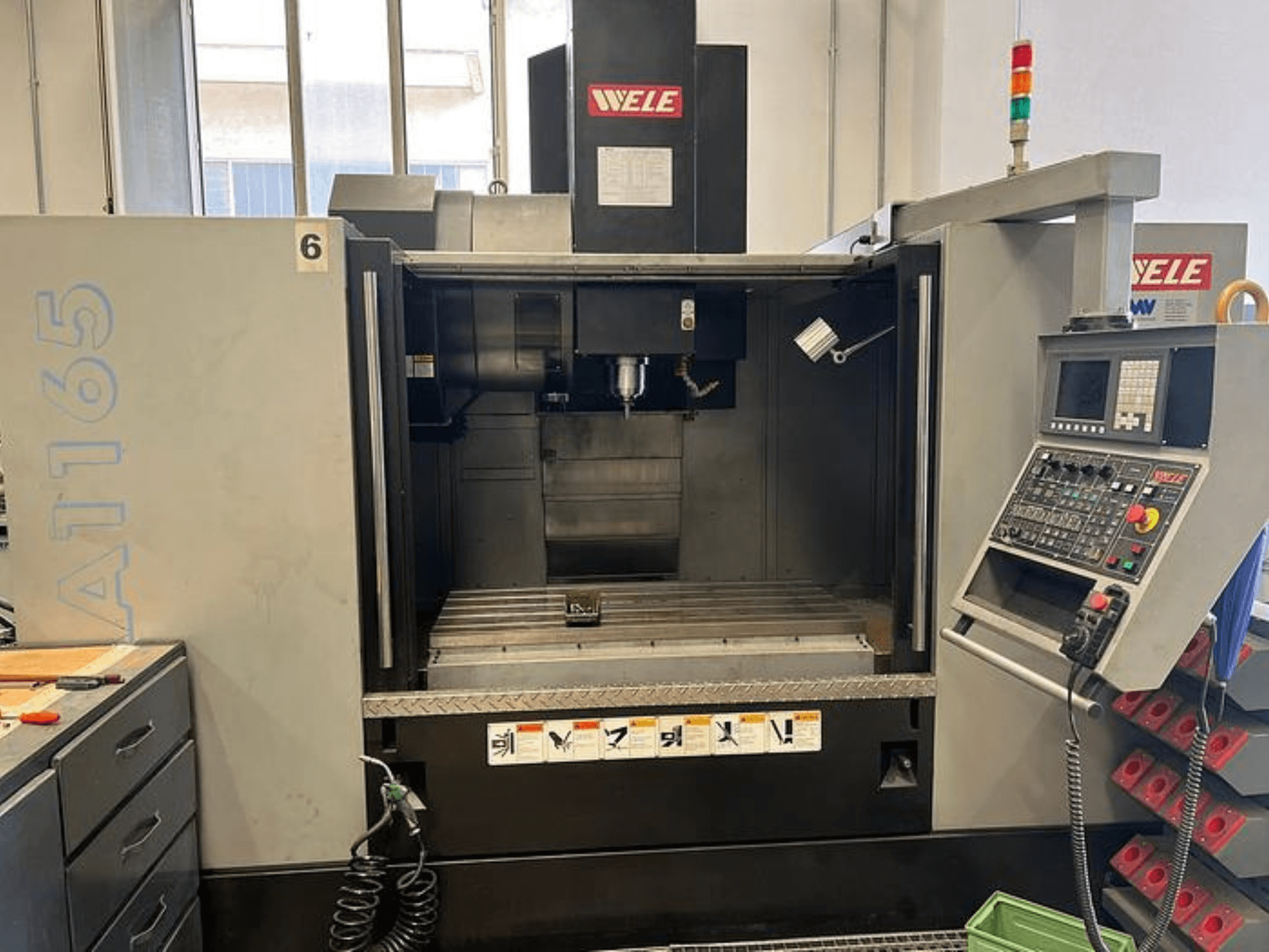 Centro di lavoro CNC WELE A165, vista frontale, con pannello di controllo, portautensili e piano di lavoro visibili. Ambientazione industriale.