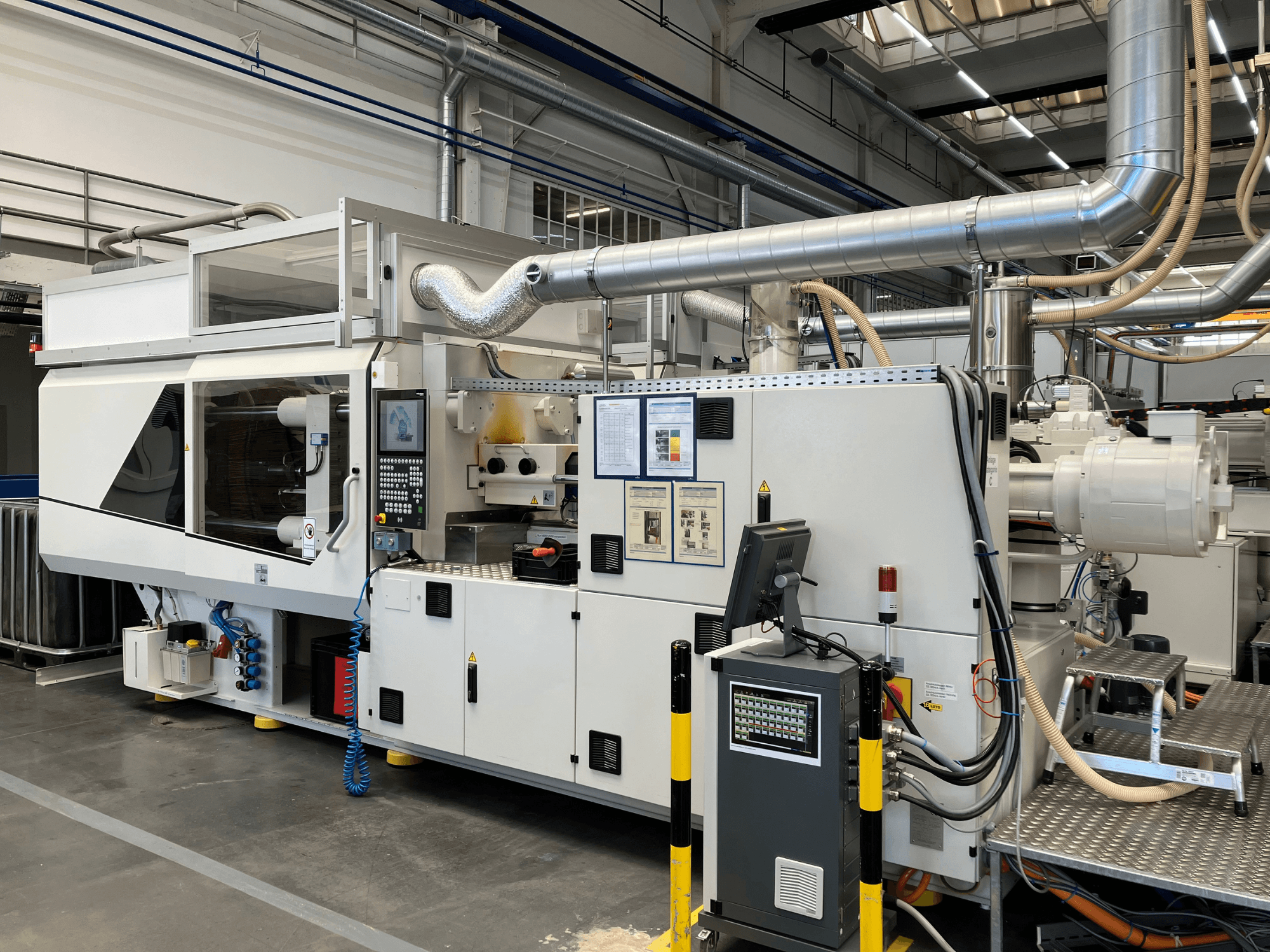 Vista frontale di una macchina industriale con pannello di controllo, tubi e schermi di visualizzazione, caratterizzata da un elegante design bianco e da dettagli tecnici.