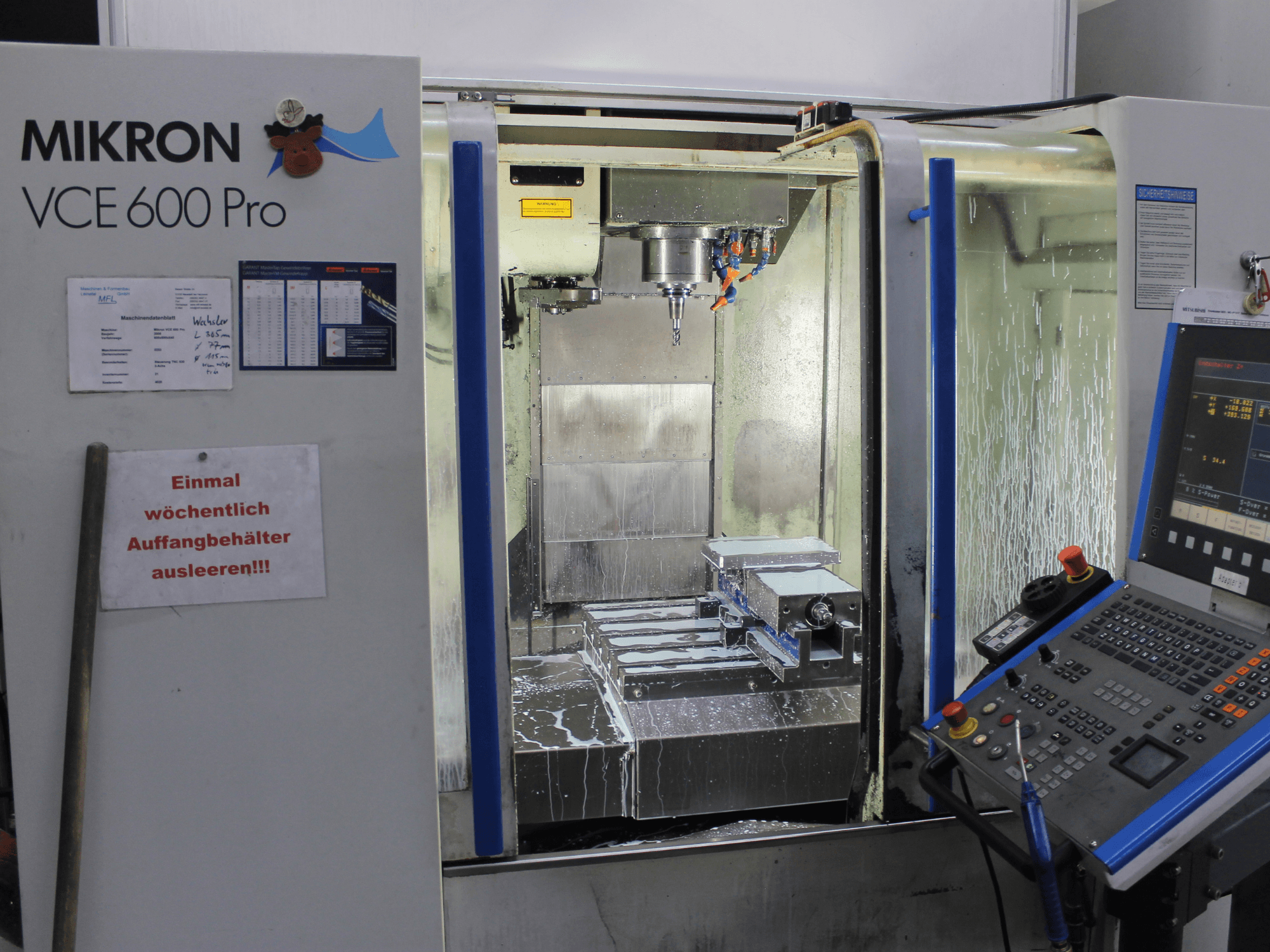 Centro di lavoro Mikron VCE 600 Pro, vista frontale, con utensili da taglio, spray refrigerante e pannello di controllo con pulsanti.