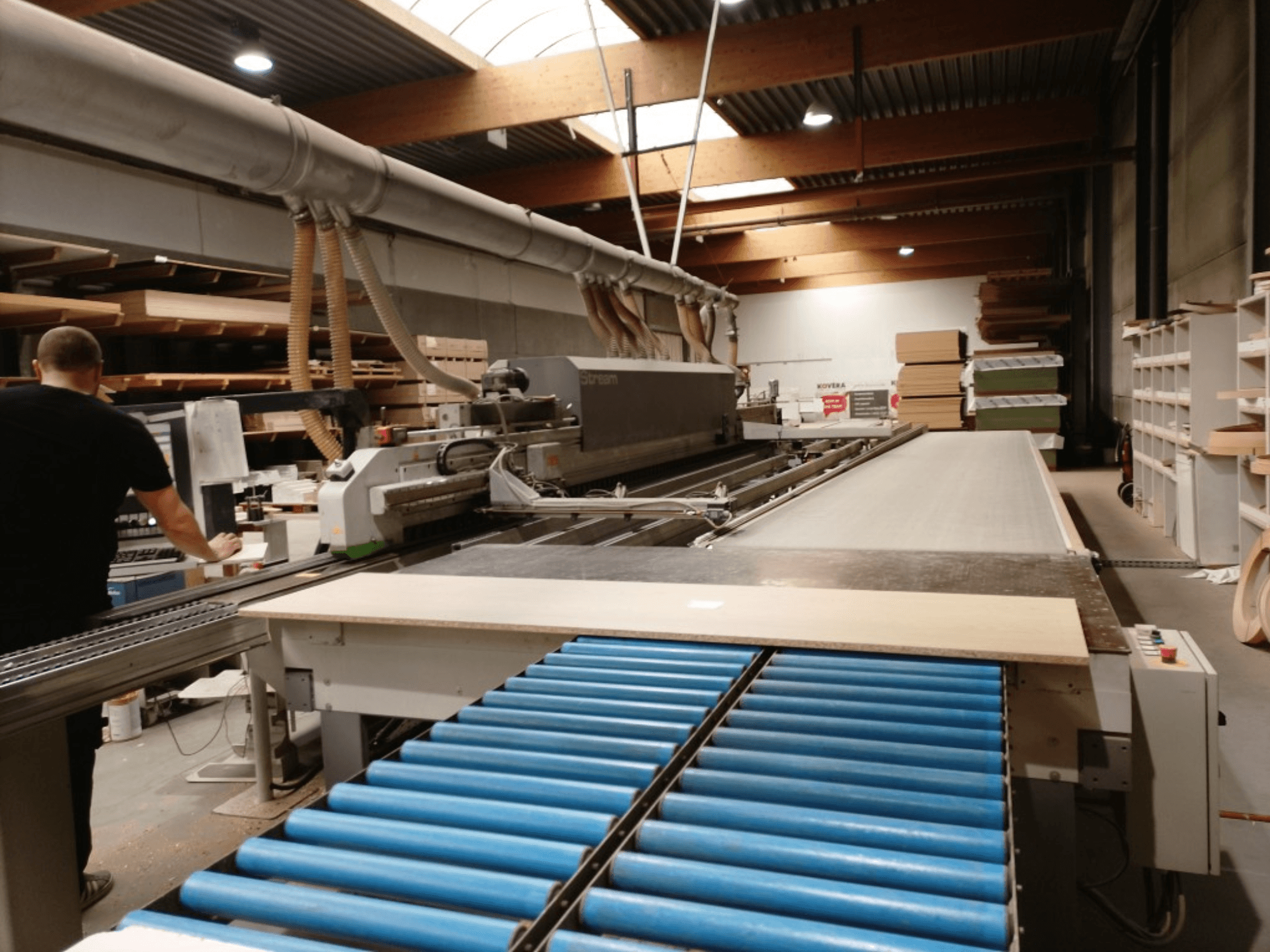 Bordatrice BIESSE Edge Stream B1, vista laterale che mostra l'operatore, i rulli blu e il pannello di legno sul trasportatore.