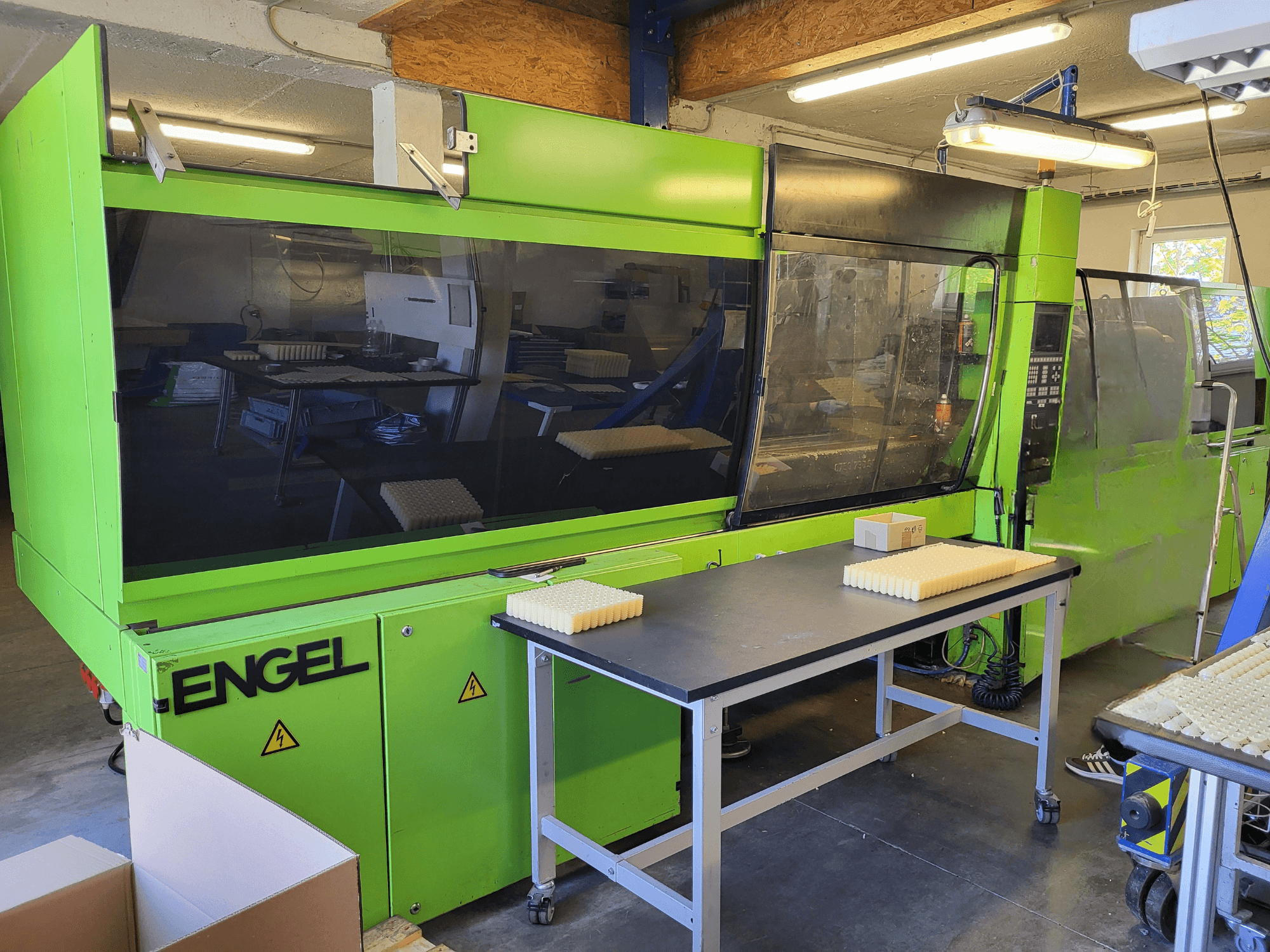 Macchina per lo stampaggio a iniezione idraulica Green Engel ES1800/300HL vista frontalmente, con i materiali impilati su un tavolo di lavoro.