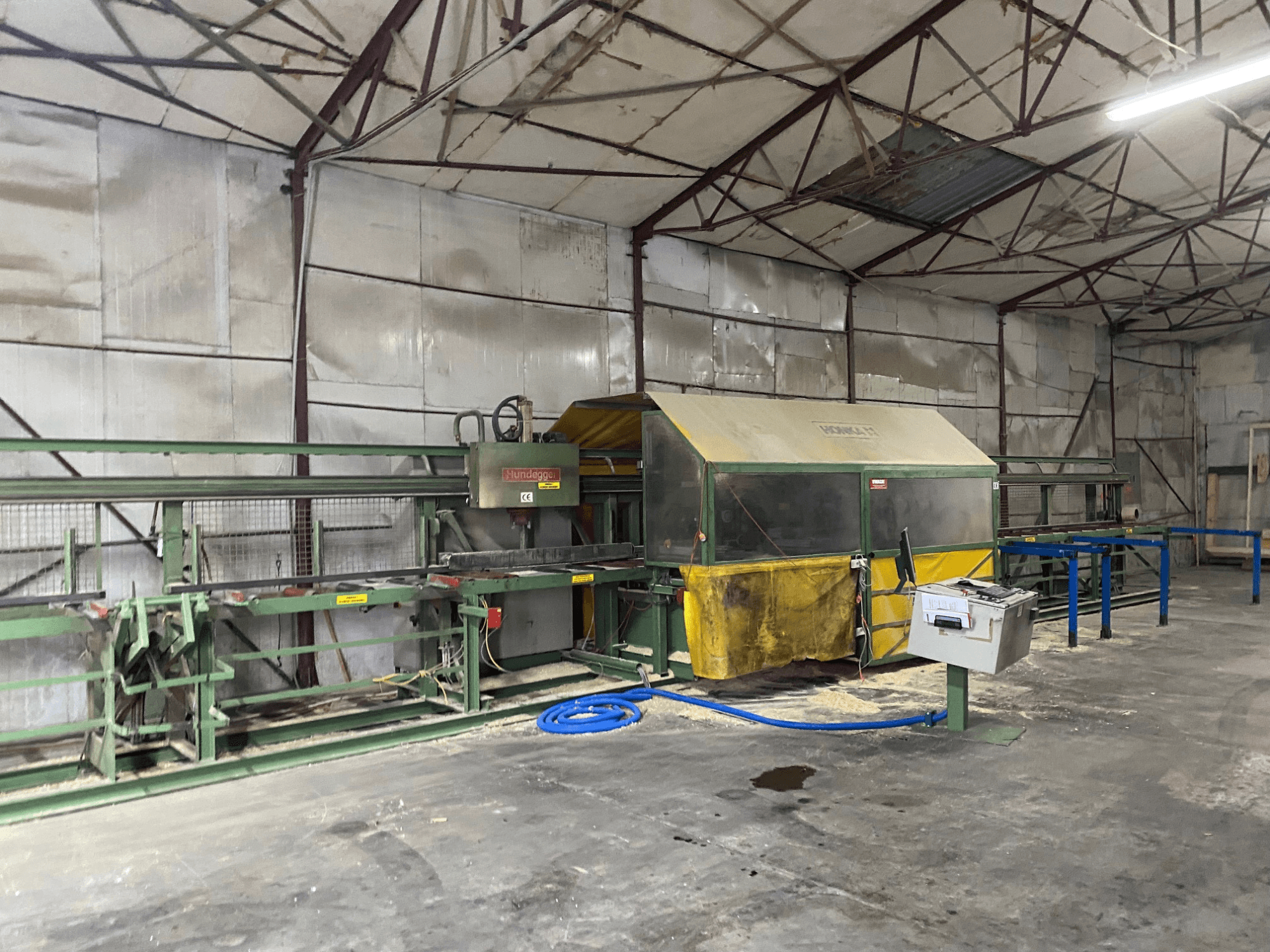 Centro di lavorazione del legno CNC HUNDEGGER K1 in un'officina, vista laterale che mostra i macchinari, i comandi e la segatura sul pavimento.