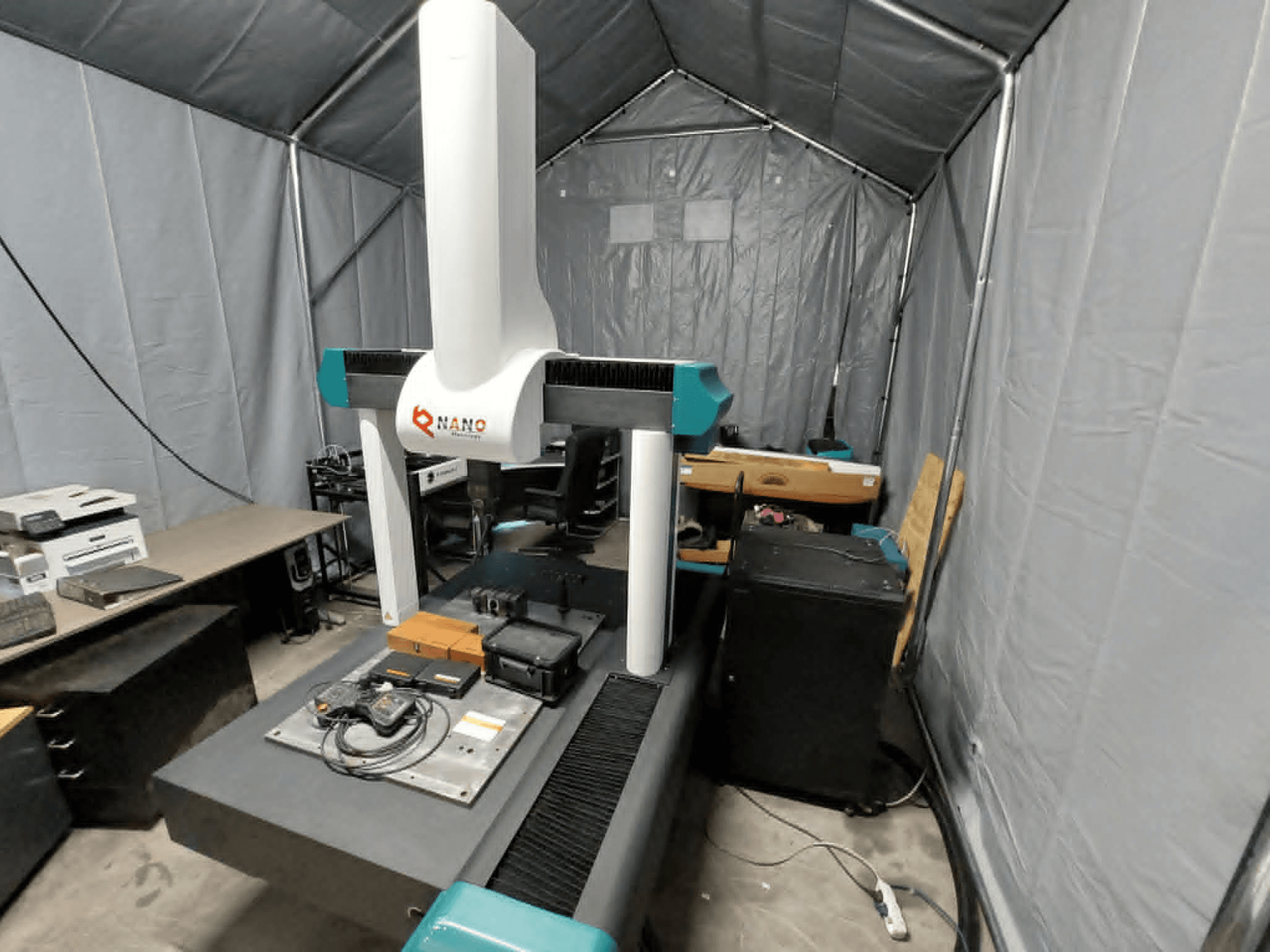 NANO METROLOGY Micr 7106 CMM in una tenda; vista frontale che mostra il braccio della macchina e la piattaforma di misura con gli accessori.