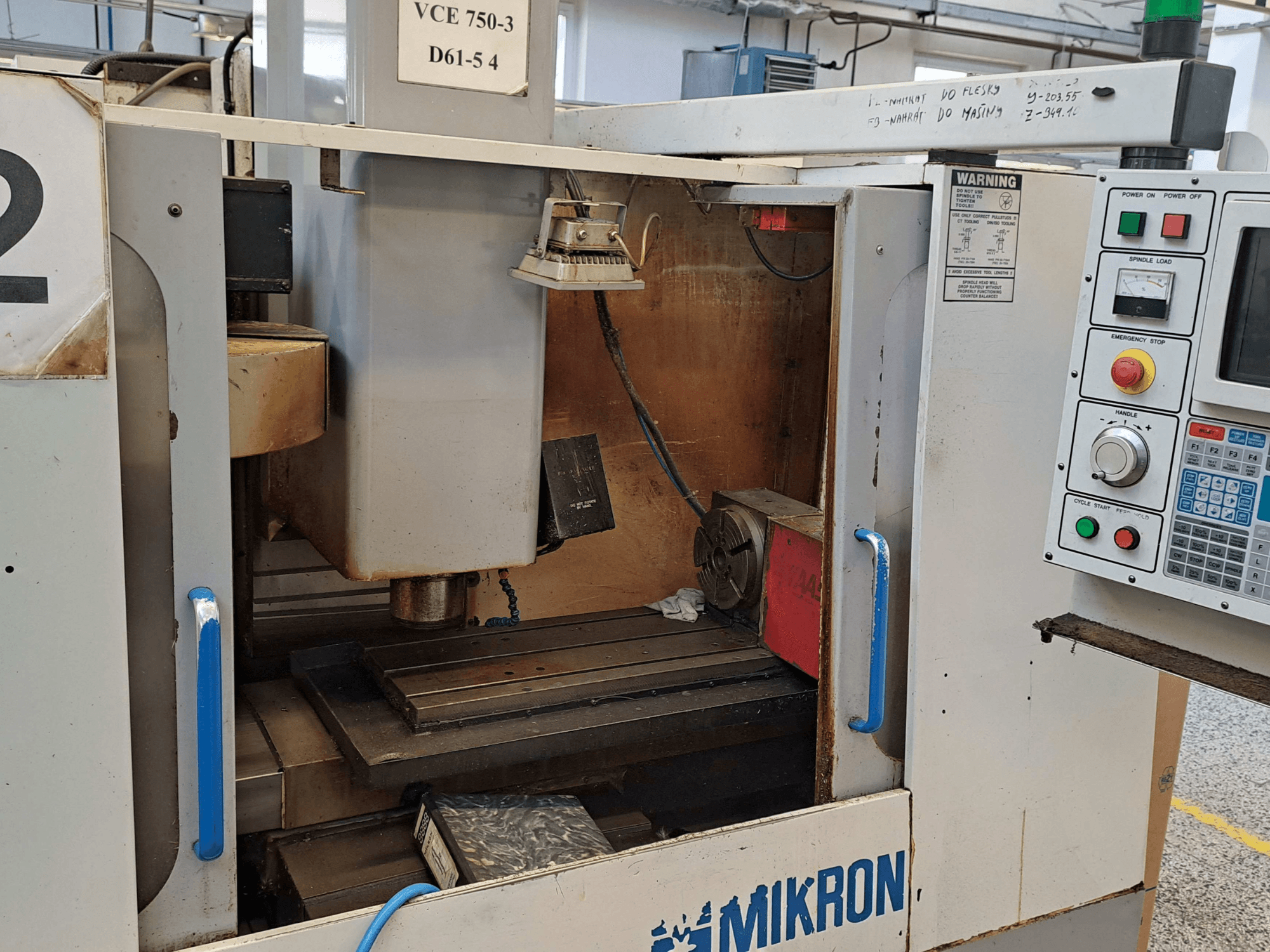 Vista frontale di una fresatrice Mikron VCE 750-3, con mandrino, pannello di controllo e piano di lavoro con dettagli tecnici.