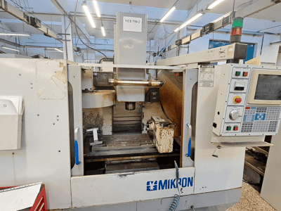 Fresatrice CNC Mikron VCE 750-2, vista frontale, con pannello di controllo e mandrino nell'area di lavorazione, presenta usura e sporcizia.