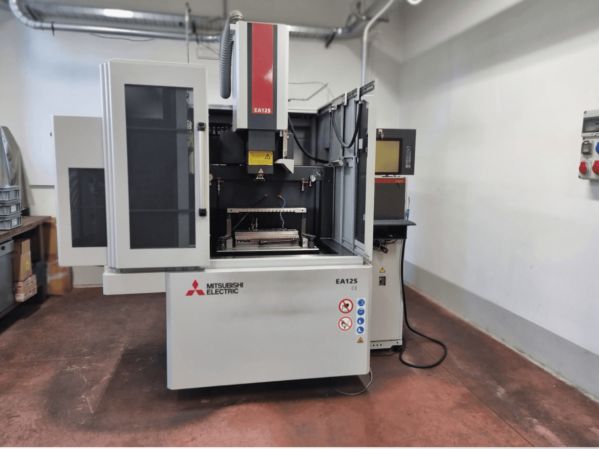 Macchina per il taglio del filo Mitsubishi Electric EA12S, vista frontale, con porte aperte, pannello di controllo ed etichette di sicurezza.
