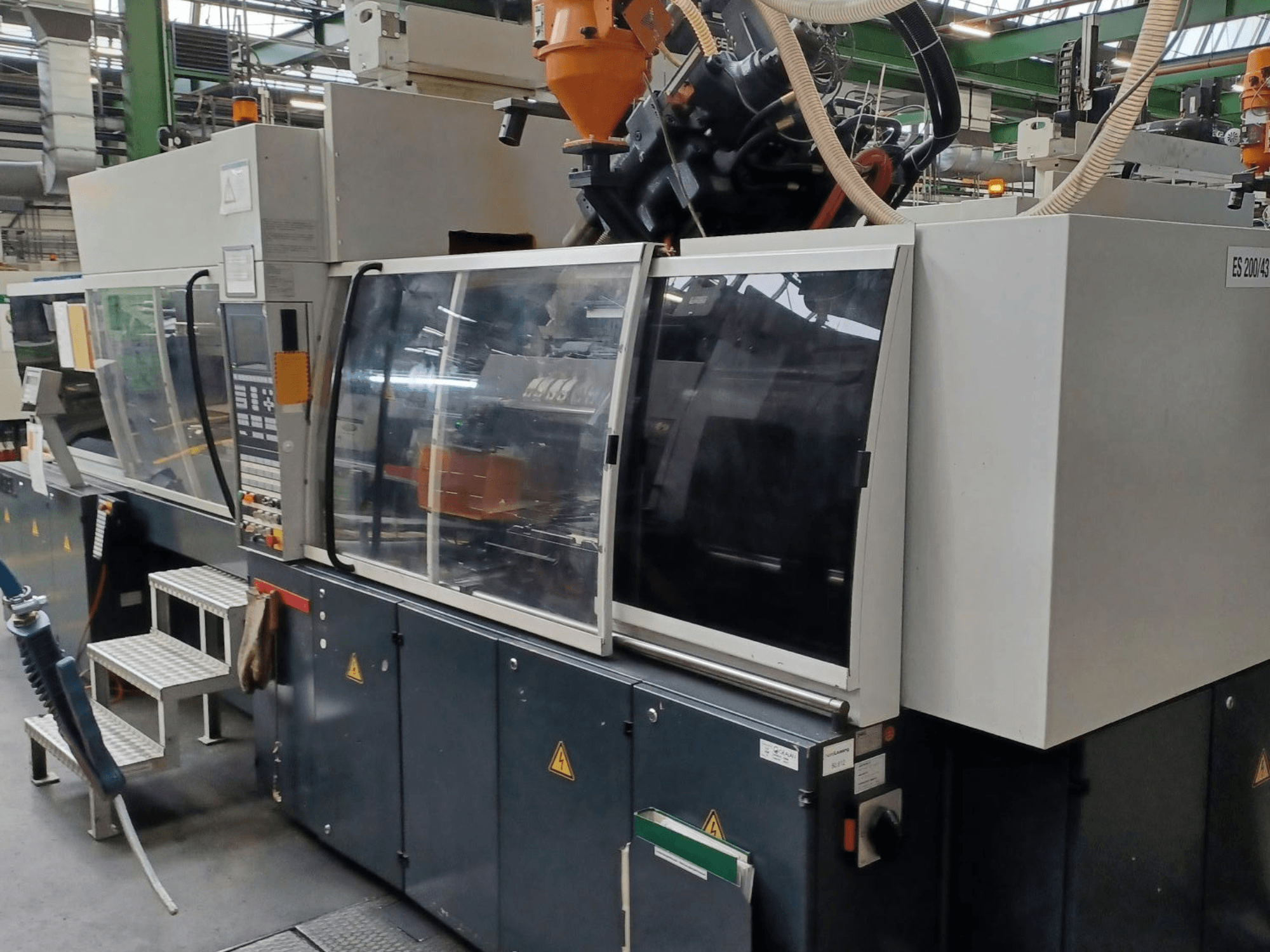 Vista frontale di una macchina per lo stampaggio a iniezione di materie plastiche, marca e modello sconosciuti, con porte di sicurezza trasparenti e pannello di controllo.