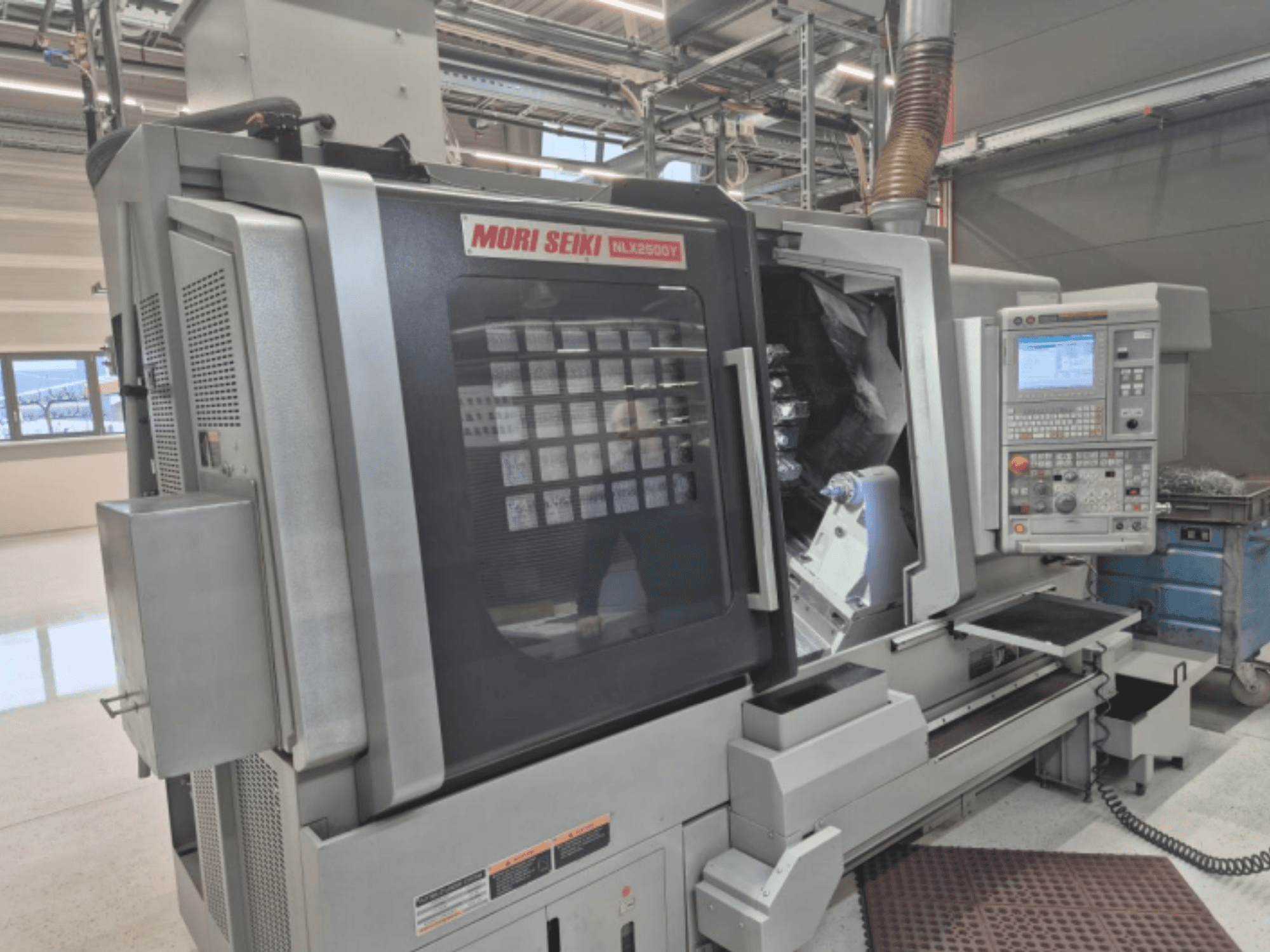 Tornio CNC MORI SEIKI NL2500Y in un ambiente di fabbrica, vista frontale che mostra il pannello di controllo e la camera del pezzo.