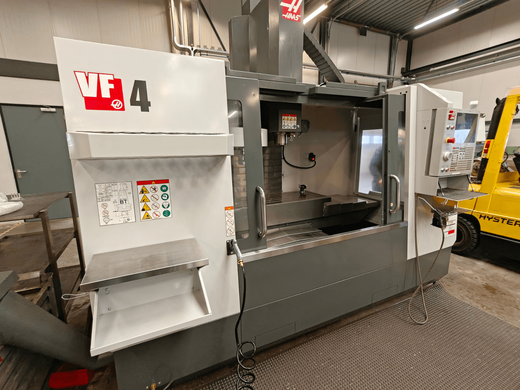 Centro di lavoro verticale HAAS VF-4, vista frontale, con pannello di controllo, area di lavoro ed etichette di sicurezza sul lato.
