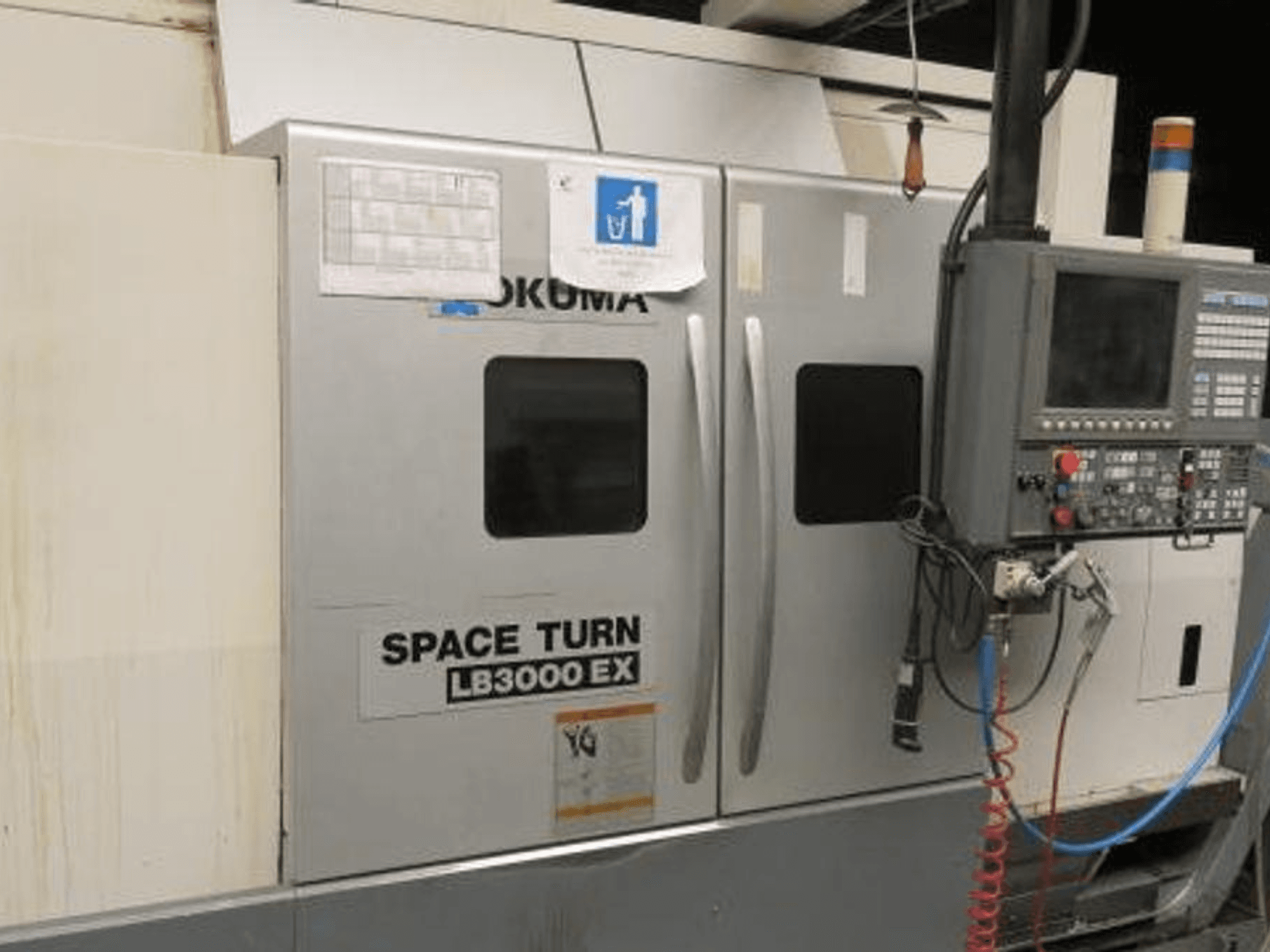 Tornio CNC Okuma Space Turn LB3000 EX, vista laterale, con pannello di controllo, due porte e cablaggio visibile.