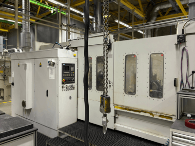 Macchina CNC industriale con pannello di controllo, vista laterale; presenta finestre, catene e componenti metallici in un ambiente di fabbrica.