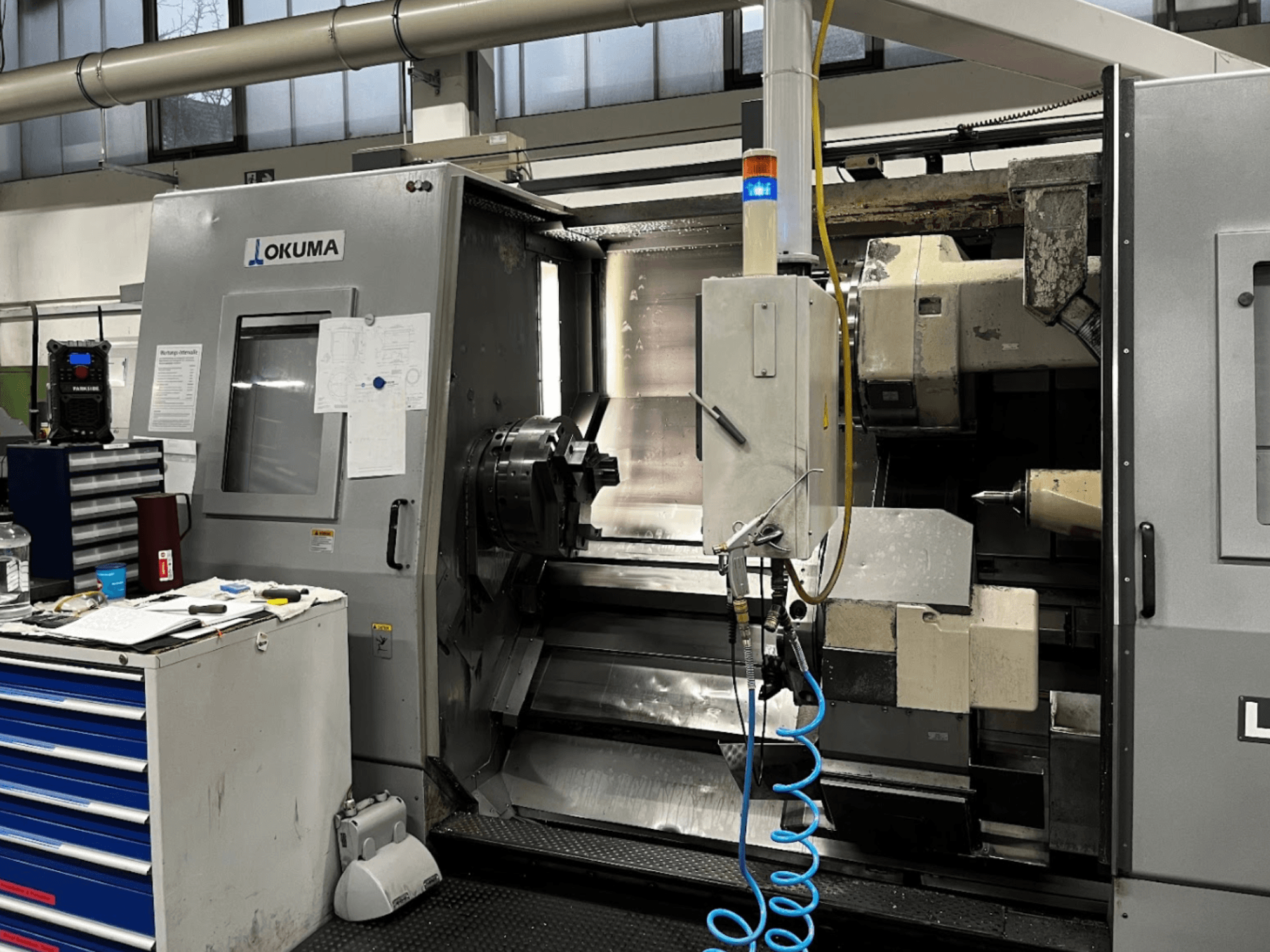 Tornio orizzontale Okuma LU35-M, vista frontale. Pannello di controllo, utensili e grande mandrino per le operazioni di lavorazione.